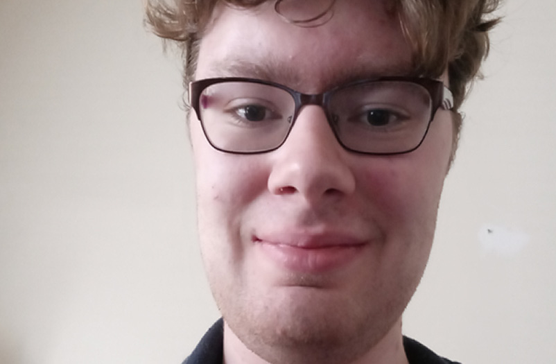 Closeup of a young man smiling wearing glasses.